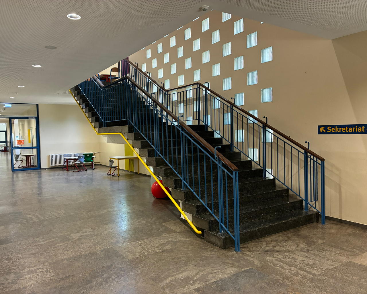 Die Eingangshalle der Schule mit der Treppe zum Obergeschoss und der Glasbausteinwand