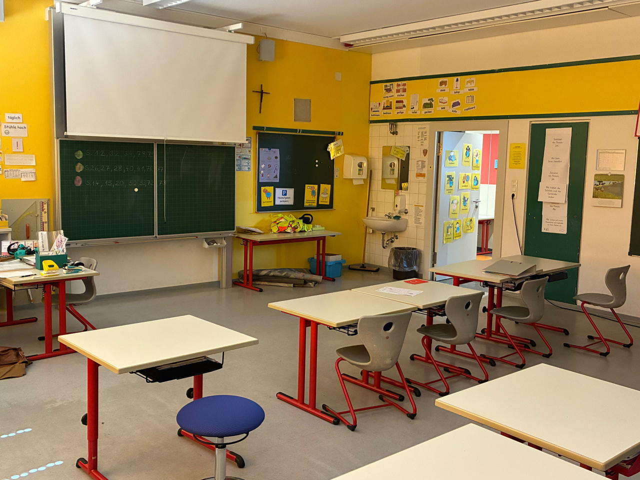 Ein Klassenzimmer mit grüner Tafel vor gelber Wand