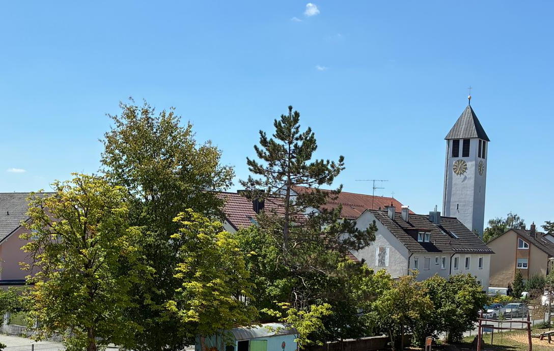 Blick vom Schulhaus über die Bäume am Pausenhof auf den Straubinger Osten mit dem Kirchturm von St. Peter